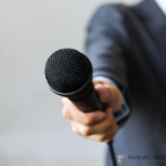 Man in suit holding microphone out to you